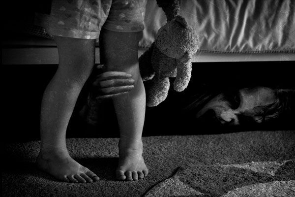 Una bruja se oculta debajo de una cama y sujeta el pie de una niña. 